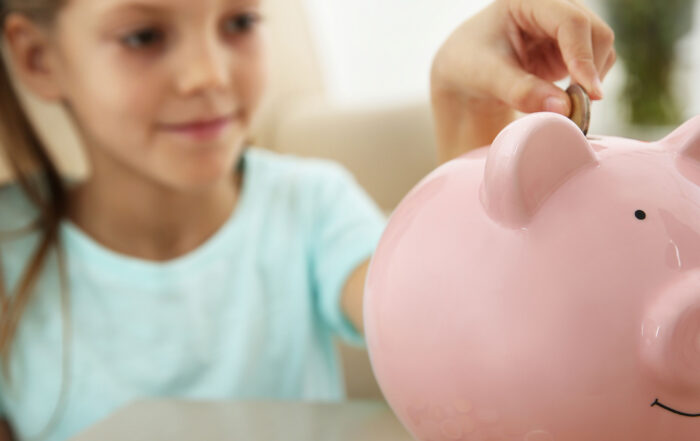 Kind wirft Geld in eine Spardose